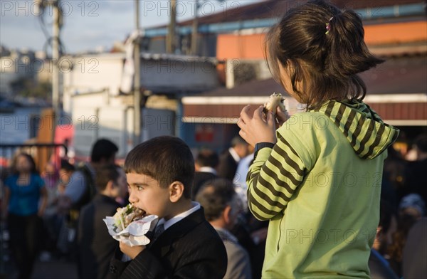 Istanbul, Turkey. Sultanahmet. Turkish boy and girl eating grilled fresh fish in bread at Kumkapi between Bosphorous and Galata Bridge. Turkey Turkish Istanbul Constantinople Stamboul Stambul City Europe European Asia Asian East West Urban Destination Travel Tourism Sultanahmet Kids Young Children Boy Girl Eating Fast Food Grilled Fish Bread Kumkapi Destination Destinations Immature Middle East South Eastern Europe Turkiye Western Asia