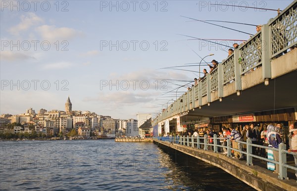 Istanbul, Turkey. Sultanahmet. View towards Galata Tower with men fishing from Galata bridge above fish restaurants below. Turkey Turkish Istanbul Constantinople Stamboul Stambul City Europe European Asia Asian East West Urban Destination Travel Tourism Sultanahmet Bosphorous Galata Bridge People Crowd Fishing Rods Men Destination Destinations Male Man Guy Middle East South Eastern Europe Turkiye Western Asia