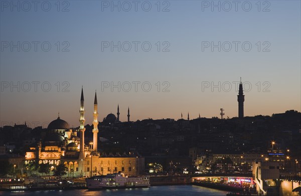 Istanbul, Turkey. Sultanahmet. The Golden Horn. The New Mosque or Yeni Camii at left the Galata Bridge and Suleymaniye Mosque at right. Buildings illuminated at dusk. Turkey Turkish Istanbul Constantinople Stamboul Stambul City Europe European Asia Asian East West Urban Skyline Destination Travel Tourism Sultanahmet Golden Horn New Mosque Yeni Camii Galata Bridge Suleymaniye Dusk Sunset Night Illuminated Skyline Minarets Water Citiscape Building Buildings Urban Architecture Destination Destinations Middle East Nightfall Twilight Evenfall Crespuscle Crespuscule Gloam Gloaming Nite South Eastern Europe Sundown Atmospheric Turkiye Western Asia