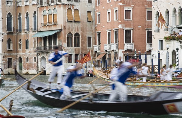 Venice, Veneto, Italy. Participants in the Regata Storico historical Regatta held annually in September in blur of movement as they approach the Rialto bridge with onlookers on the balconies of canalside buildings behind. Teams represent Sestiere districts of Venice in traditional races. Italy Italia Italian Venice Veneto Venezia Europe European City Regata Regatta Gondola Gondola Gondolas Gondolier Boat Architecture Exterior Water Blur Blurred Movement Classic Classical Destination Destinations History Historic Holidaymakers Older Southern Europe Tourism Tourist