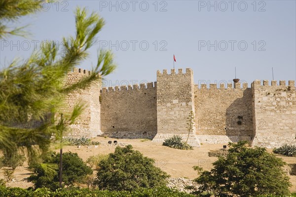 Selcuk, Izmir Province, Turkey. Site of the 6th century Basilica of St. John the Apostle below section of crenellated wall and towers with trees and bushes in foreground. Turkey Turkish Eurasia Eurasian Europe Asia Turkiye Izmir Province Selcuk Basilica St Saint John Apostle Crenellated Wall Walls Tower Towers Destination Destinations European History Historic Middle East South Eastern Europe Western Asia