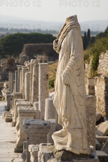 Selcuk, Izmir Province, Turkey. Ephesus. Headless statue on plinth in line of ruined pillars and empty pedestals in antique city of Ephesus on the Aegean sea coast. Turkey Turkish Eurasia Eurasian Europe Asia Turkiye Izmir Province Selcuk Ephesus Ruin Ruins Roman Column Columns Facde Ancient Architecture Masonry Rock Stone Statue Figure Headless Destination Destinations European History Historic Middle East South Eastern Europe Water Western Asia