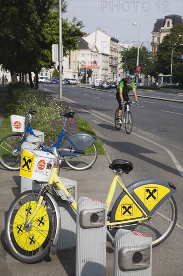 Vienna, Austria. Neubau District. Bicycles for use in city centre with approaching cyclist on road behind. Austria Austrian Republic Vienna Viennese Wien Europe European City Capital Neubau District Urban Transport Bicycle Bike Bicycles Bikes Cycle Cyclist Pay Hire Rent Center Destination Destinations One individual Solo Lone Solitary Osterreich Viena Western Europe