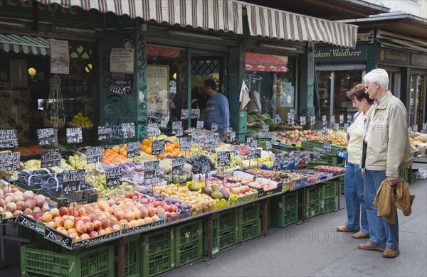 Vienna, Austria. The Naschmarkt. Customers selecting fresh fruit from display on market stall that includes nectarines peaches plums grapes and mangoes. Austria Austrian Republic Vienna Viennese Wien Europe European City Capital Naschmarkt Market Display Fresh Food Fruit Vegetables Veg Vegetable Stall Shop Store Destination Destinations Osterreich Viena Western Europe