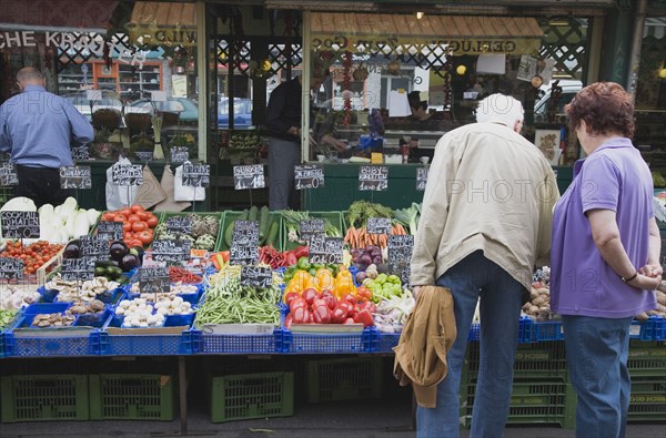 Vienna, Austria. The Naschmarkt. Customers selecting fresh fruit from display on stall that includes aubergines mushrooms peppers and carrots. Austria Austrian Republic Vienna Viennese Wien Europe European City Capital Naschmarkt Market Display Fresh Food Fruit Vegetables Veg Vegetable Stall Shop Store Destination Destinations Osterreich Viena Western Europe