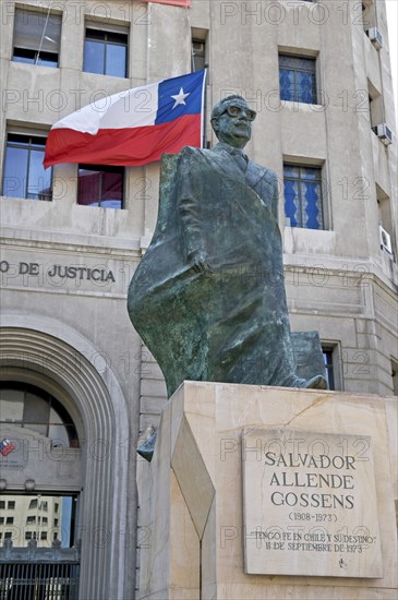 Santiago, Chile. Statue of President Salvador Allende in Plaza de la Constitucion or Constitution Square opposite the Palacio de la Moneda Presidential Palace where he was killed in a military coup. Chilean flag and entrance of the Ministry of Justice. Chile Chilean South America American Hispanic Santiago City Cityscape Urban Statue President Salvador Allende Gossens Plaza de la Consticion Constitution Square Ministry Justice Flag Offical Administrative Offical Government Architecture Building Destination Destinations Latin America Latino South America Southern