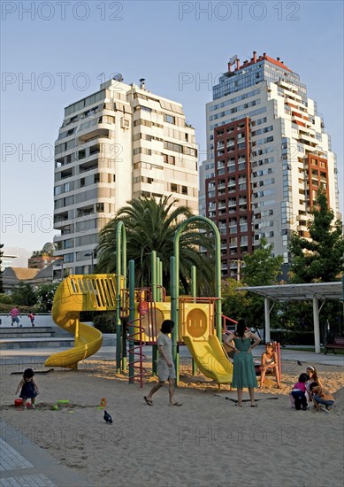 Santiago, Chile. Children playing in the sand while their mothers watch at a playground in Plaza Peru in Vitacura Santiagos plushest neighbourhood highrise apartment blocks beyond. American Chilean Destination Destinations Flat Hispanic Kids Latin America Latino Peruvian South America Southern