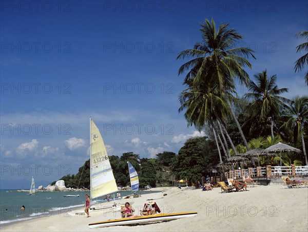 Batu Ferringhi, Penang, Malaysia. Beach scene with tourists sunbathing. Malaysia Malaysian Palmenstrand Penang Batu Ferringhi Beach Palm Tree Sand Shore Coast Sea Water Sail Boat Relax Hoby Cat Catamaran Tourist Tourist Sunbathing Beach Holiday Vacation Travel Asian Blue Destination Destinations Holidaymakers Sand Sandy Beaches Tourism Seaside Shore Tourist Tourists Vacation Sightseeing Southeast Asia Southern Sunbather Water