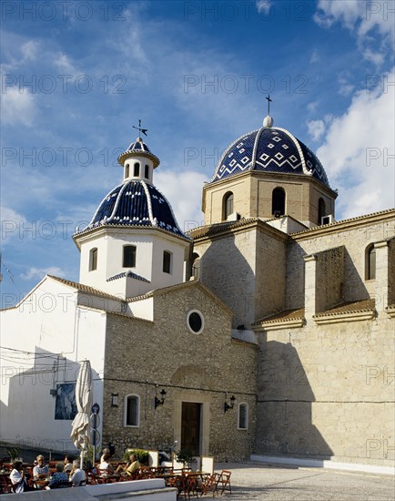 Valencia, Costa Blanca, Spain. Alicante Province Altea. Church with blue tiled roof in the square with tourists sat outsde cafe in foreground. Spain Spanish Europe European Costa Blanca Valencia Alicante Province Altea Town Architecture Religious Religion Christian Christianity Blue Tiled Roof Dome Domes Tourists Square Cafe Bar Bistro Clouds Cloud Sky Destination Destinations Espainia Espana Espanha Espanya Hispanic Holidaymakers Religion Religious Christianity Christians Restaurant Southern Europe Tourism