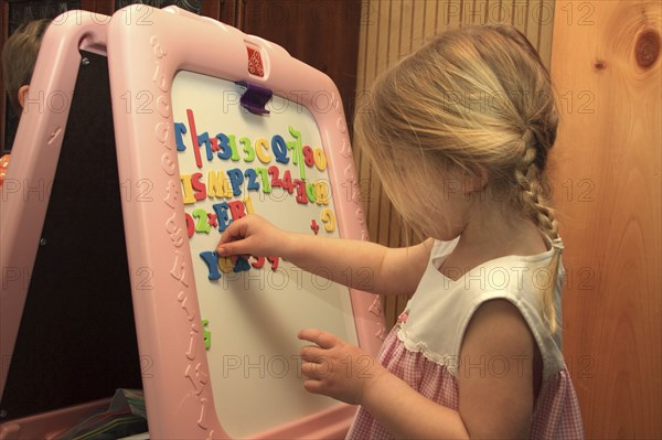 Young girl Sarah Bleau using magnetic letters on dry erase board in Keene New Hampshire. Education Learn Learning Educational Toys Toy Aid Tool Wipeboard Erase Magnetic Letter Letters Play Playing Primary School MR Model Release Released Sarah Bleau Spell Spelling Number Numbers Numeration Counting Counts American Immature Kids Lessons North America Northern One individual Solo Lone Solitary Teaching United States of America