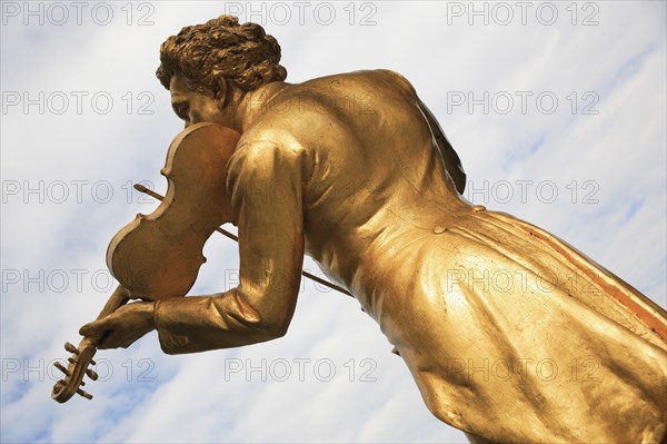 Vienna, Austria. Part view of Johann Strauss statue in the Stadtpark. Austria Austrian Vienna Wien Viennese Republic Austro-Bavarian Wean Europe European City Capital Travel Destination Art Statue Stadpark Park Public Johann Strauss Violin Gold Blue Clouds Cloud Sky Color Destination Destinations Osterreich Viena Western Europe