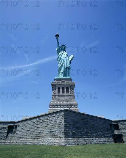 New York, New York State, USA. Statue of Liberty. Green statue with gold torch flame stone wall and grass. American Destination Destinations North America Northern United States of America