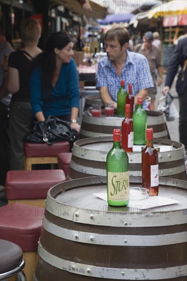 Vienna, Austria. Young couple having glass of Federweisser wine in the fermentation stage known as Sturm in Austria seated at outside table made from a barrel. Due to the carbonic acid Federweisser tastes quite refreshing not unlike a grape lemonade or a sweet sparkling wine. Austria Austrian Republic Vienna Viennese Wien Europe European City Capital Market Drink Drinks Alcohol Wine Federweisser Fermentation Sturm Barrel Barrels Couple Destination Destinations Immature Osterreich Viena Vino Vin Alcohol Grape Winery Drink Western Europe