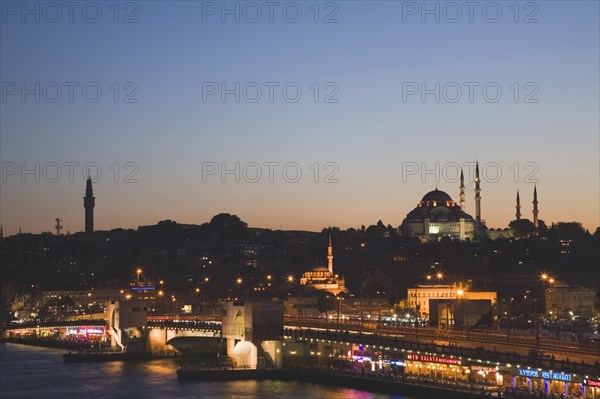 Istanbul, Turkey. Sultanahmet. The Golden Horn. The New Mosque or Yeni Camii at left the Galata Bridge and Suleymaniye Mosque at right illuminated at dusk. Turkey Turkish Istanbul Constantinople Stamboul Stambul City Europe European Asia Asian East West Urban Skyline Destination Travel Tourism Sultanahmet Golden Horn New Mosque Yeni Camii Galata Bridge Suleymaniye Dusk Sunset Night Illuminated Skyline Minarets Water Citiscape Building Buildings Urban Architecture Destination Destinations Middle East Nightfall Twilight Evenfall Crespuscle Crespuscule Gloam Gloaming Nite South Eastern Europe Sundown Atmospheric Turkiye Western Asia