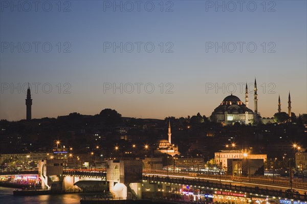 Istanbul, Turkey. Sultanahmet The Golden Horn. The New Mosque or Yeni Camii at left the Galata Bridge and Suleymaniye Mosque at right illuminated at dusk. Turkey Turkish Istanbul Constantinople Stamboul Stambul City Europe European Asia Asian East West Urban Skyline Destination Travel Tourism Sultanahmet Golden Horn New Mosque Yeni Camii Galata Bridge Suleymaniye Dusk Sunset Night Illuminated Skyline Minarets Water Citiscape Building Buildings Urban Architecture Destination Destinations Middle East Nightfall Twilight Evenfall Crespuscle Crespuscule Gloam Gloaming Nite South Eastern Europe Sundown Atmospheric Turkiye Western Asia