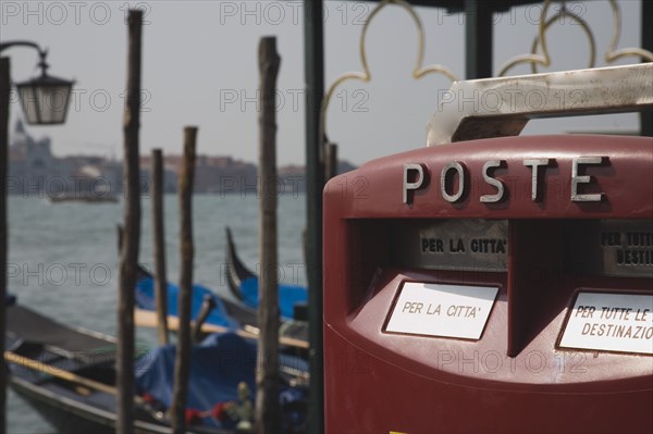 Venice, Veneto, Italy. Post box with gondolas moored on the Grand Canal behind. Italy Italia Italian Venice Veneto Venezia Europe European City Water Gondolas Gondola Mail Box Post Red Poste Color Destination Destinations Southern Europe