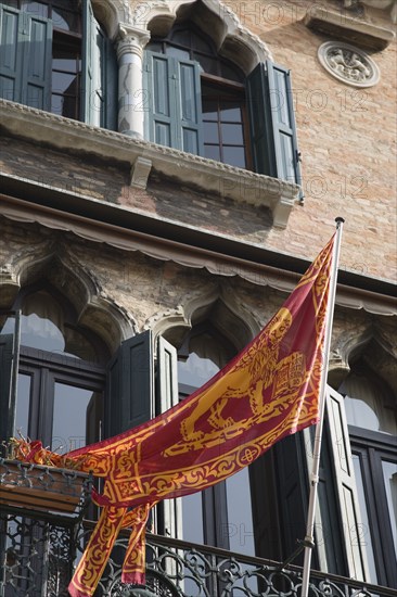 Venice, Veneto, Italy. Centro Storico Republic of Venice flag depicting winged lion of St. Mark on facade of building with islamic influenced window arches. Italy Italia Italian Venice Veneto Venezia Europe European City Centro Storico Republic Flag Winged Lion Window Windows Balcony Facade Architecture Destination Destinations History Historic Southern Europe