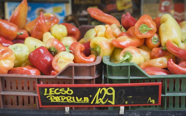 Budapest, Pest County, Hungary. Crate of red orange and yellow Capsicum annuum or Bell Chili peppers also known as paprika in reference to the spice produced in dried and ground form on stall with price label attached. Hungary Hungarian Europe European East Eastern Buda Pest Budapest City Vegetable Vegatbles Fuit Chili Chillis Chillies Pepper Peppers Red Capsicum Annuum Bell Paprika Color Destination Destinations Eastern Europe