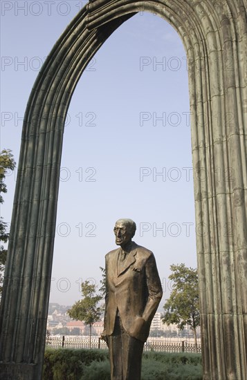 Budapest, Pest County, Hungary. Statue of standing man beneath arch beside the River Danube. Hungary Hungarian Europe European East Eastern Buda Pest Budapest City Art Statue Arch Man Male Figure Blue Destination Destinations Eastern Europe Male Men Guy