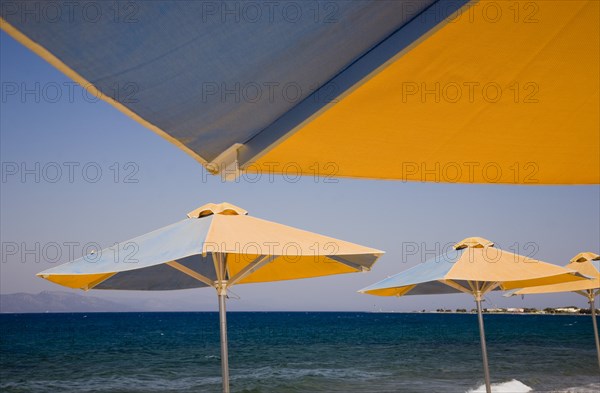 Kos, Dodecanese Islands, Greece. Blue and yellow striped parasols on beach outside Kos Town. Greece Greek Europe European Vacation Holiday Holidays Travel Destination Tourism Ellas Hellenic Docecanese Kos Sea Umbrella Umbrellas Parasol Parasols Blue Orange Color Destination Destinations Ellada Sand Sandy Beaches Tourism Seaside Shore Tourist Tourists Vacation Southern Europe Water