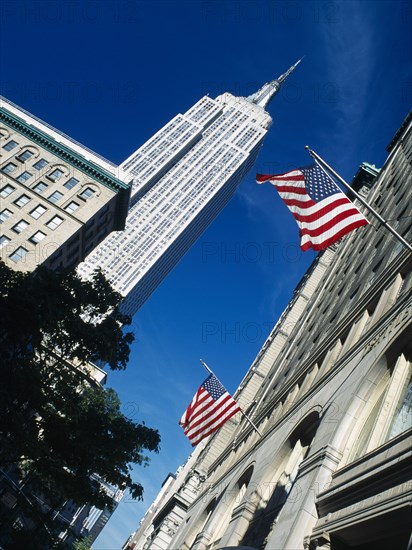 Manhattan, New York, USA. Angled view looking up at the Empire State Building and building facades flying American flags on 5th Avenue North America United States of America