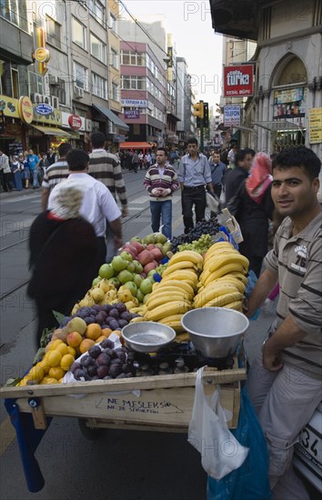 Istanbul, Turkey. Sultanahmet. Fresh fruit stall beside tramway on busy street. Turkey Turkish Istanbul Constantinople Stamboul Stambul City Europe European Asia Asian East West Urban Destination Travel Tourism Sultanahmet Street Market Stall Vendor Fruit Busy People Crowded Crowd Destination Destinations Middle East South Eastern Europe Turkiye Western Asia