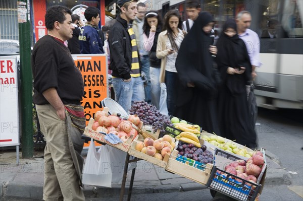 Istanbul, Turkey. Sultanahmet. Two women wearing burqa and veil passing fresh fruit stall with male vendor on busy street beside tramway. Turkey Turkish Istanbul Constantinople Stamboul Stambul City Europe European Asia Asian East West Urban Destination Travel Tourism Sultanahmet Market Market Vendor Vendor Fruit Busy People Crowded Crowd 2 Cultural Cultures Destination Destinations Female Woman Girl Lady Middle East Order Fellowship Guild Club Religious South Eastern Europe Turkiye Western Asia