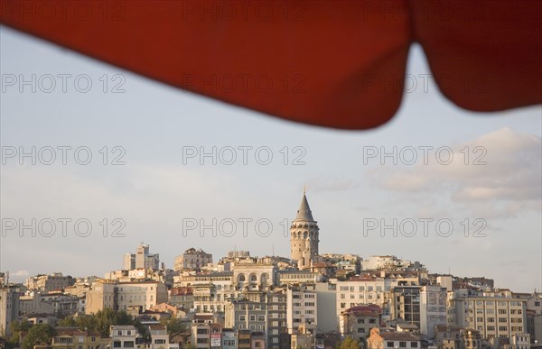 Istanbul, Turkey. Sultanahmet. View to Galata Tower from shade of red canopy alongside Galata bridge. Turkey Turkish Istanbul Constantinople Stamboul Stambul City Europe European Asia Asian East West Urban Destination Travel Tourism Sultanahmet Bosphorous Galata Tower Cityscape Rooftops Skyline Red Canopy Blue Citiscape Building Buildings Urban Architecture Clouds Cloud Sky Color Destination Destinations Middle East South Eastern Europe Turkiye Western Asia