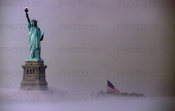 Liberty Island, New York, USA. Statue of Liberty and Stars and Stripes Flag on misty morning. USA United State States America American New York City Liberty Island Statue Copper Metal Figure Female Green Torch Mist Fog Moody Flag Stars Stripes History Historic North America Northern Surly United States of America