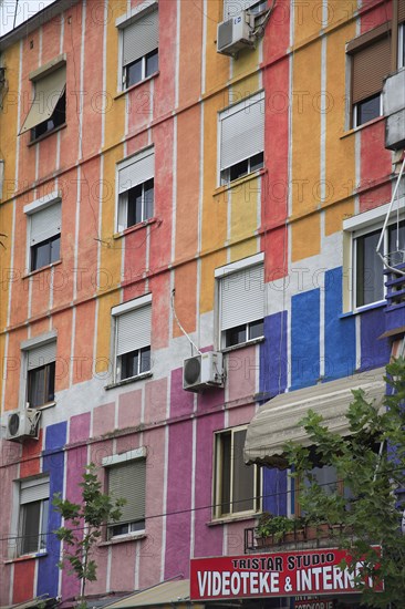 Albania, Tirane, Tirana, Part view of exterior facade of apartment block painted in brightly coloured stripes with multiple windows. Sign for Tristar Studio  video and internet business below.