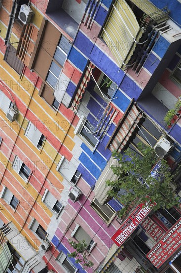 Albania, Tirane, Tirana, Angled part view of apartment block painted in brightly coloured stripes with multiple windows and balconies. Sign for Tristar Studio video and internet services below.