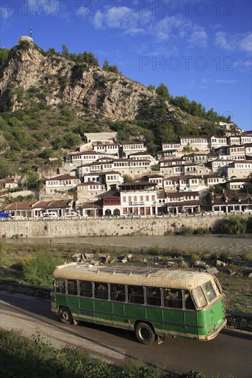 Albania, Berat, Traditional Ottoman buildings on hillside above the River Osum with local bus in foreground.