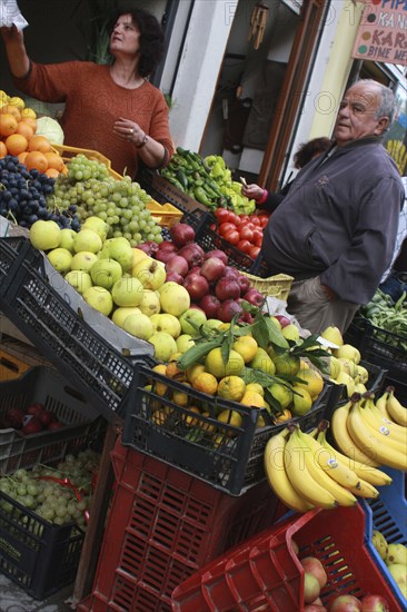 Albania, Berat, Vendor and customer beside display of fruit outside grocers shop.