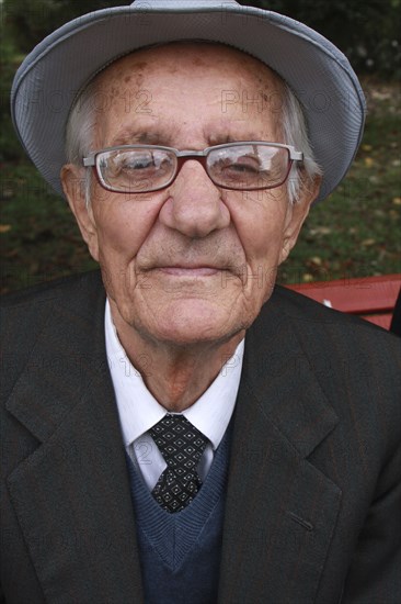 Albania, Berat, Head and shoulders portrait of an elderly man wearing hat and glasses  looking straight to camera.