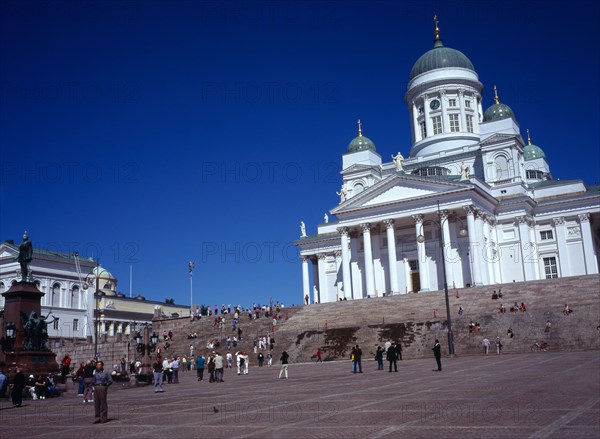 Finland, Helsinki, Senate Square and Lutheran Cathedral.  White exterior facade in neo-classical style with green domed roof and statues  at top of flight of steps with crowds of visitors.