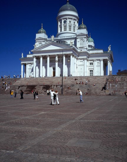 Finland, Helsinki, Senate Square and Lutheran Cathedral.  White exterior facade in neo-classical style with green domed roof and statues  above flight of steps and visitors.