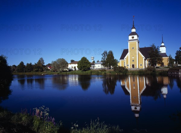 Finland, Vaasanlaani, Nykarle, Village church beside the River Lapuanjoki.  Cream and white painted exterior with clock tower reflected in the water.