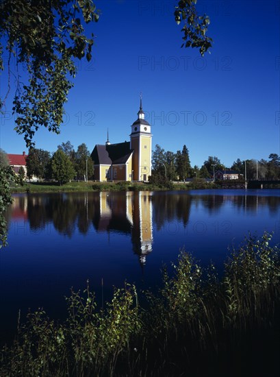 Finland, Vaasanlaani, Nykarle, Village church beside the River Lapuanjoki.  Cream and white painted exterior with clock tower reflected in the water.