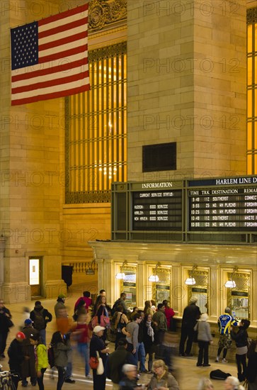 USA, New York, New York City, Manhattan  Grand Central Terminal railway station with passengers buying tickets from ticket booths in the Main Concourse beneath the American Stars and Stripes flag hanging from the ceiling.