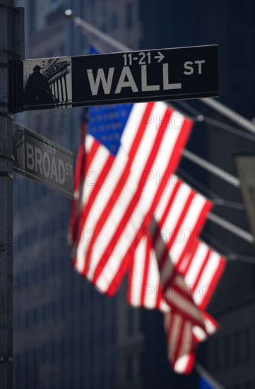 USA, New York, New York City, Manhattan  Road signs for Wall Street and Broad Street with American Stars and Stripes flags flying from the Stock Exchange building.