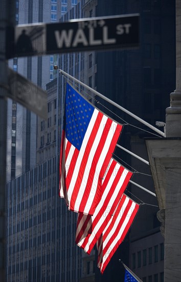 USA, New York, New York City, Manhattan  Road signs for Wall Street and Broad Street with American Stars and Stripes flags flying from the Stock Exchange building.