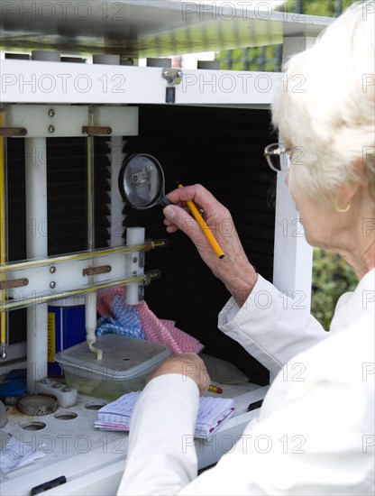 Climate, Weather, Measurements, Female weather observer using a magnifying glass to take readings from the wet-bulb thermometer or hygrometer which measures relative humidity in the Stevensons Screen cabinet at Bognor Regis weather station.