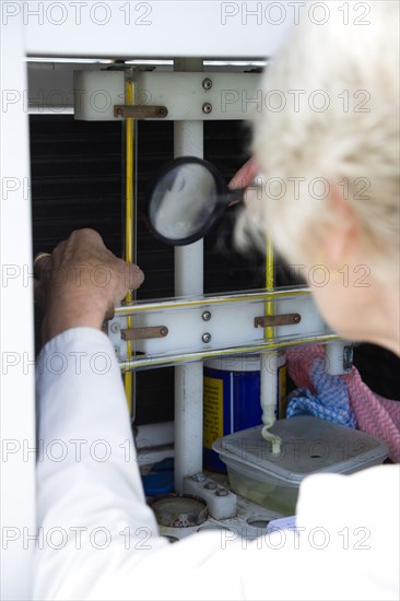Climate, Weather, Measurements, Female weather observer using a magnifying glass to take readings from the dry-bulb thermometer which measures relative humidity in the Stevensons Screen cabinet at Bognor Regis weather station.