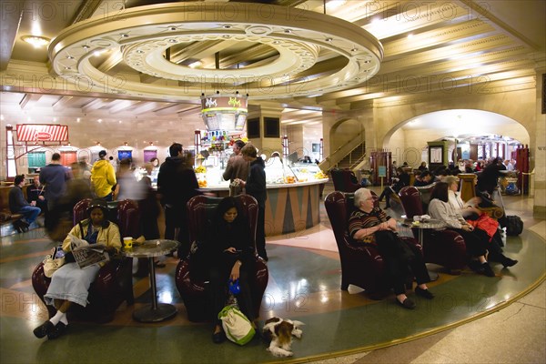 USA, New York, New York City, Manhattan  Grand Central Terminal Station Passengers sitting in armchairs or buying food and drinks from one of the central counters in the dining concourse on the lower level.