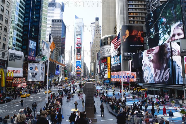 USA, New York, New York City, Manhattan  People walking in Times Square at the junction of 7th Avenue and Broadway below buildings with advertising on large video screens.