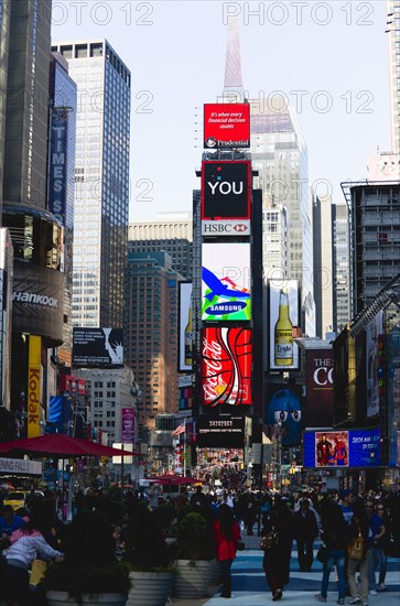 USA, New York, New York City, Manhattan  People walking in Times Square at the junction of 7th Avenue and Broadway below buildings with advertising on large video screens.