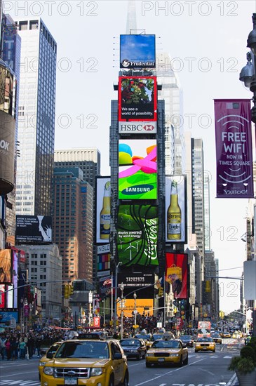 USA, New York, New York City, Manhattan  People walking in Times Square at the junction of 7th Avenue and Broadway below buildings with advertising on large video screens with yellow taxi cabs driving down 7th Avenue.