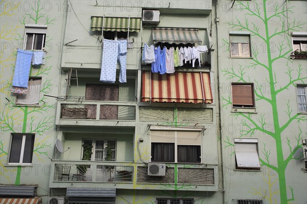 Albania, Tirane, Tirana, Detail of exterior facade of apartment block painted with tree forms in green and yellow with washing hanging from balconies and window ledge.