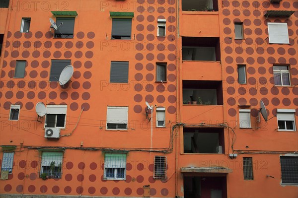 Albania, Tirane, Tirana, Part view of exterior facade of apartment block painted orange with pattern of red painted circles. Multiple windows  satelite dishes  balconies.
