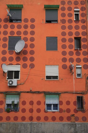 Albania, Tirane, Tirana, Detail of exterior facade of apartment block painted orange with pattern of red circles  multiple windows and satelite dishes.